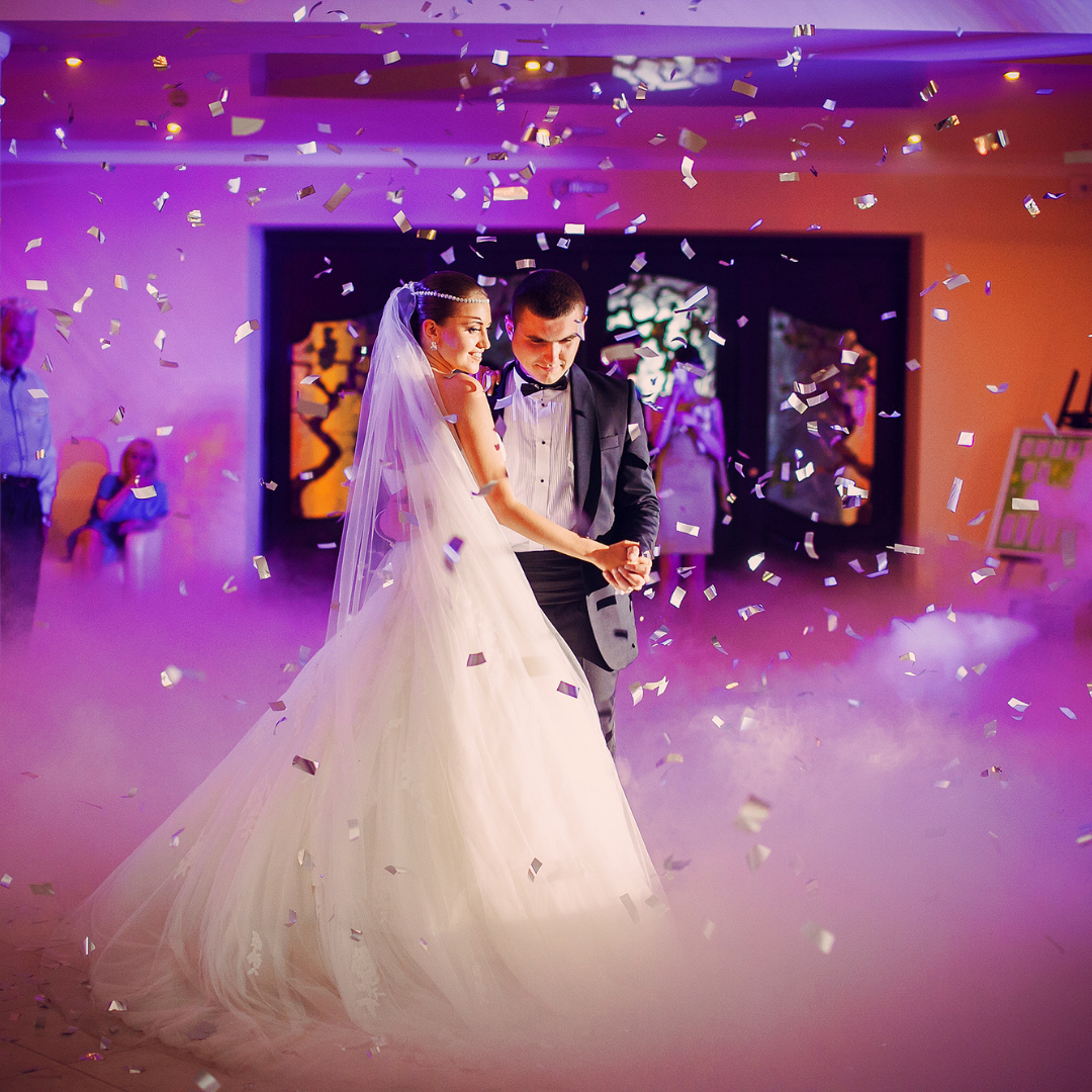 Couple dancing at their wedding ceremony in a room with confetti falling from the ceiling.